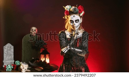 Creepy female model doing hush gesture to keep secret, wearing santa muerte costume and showing slience mute and secrecy sign with finger over lips. Holy dios de los muertos holiday.