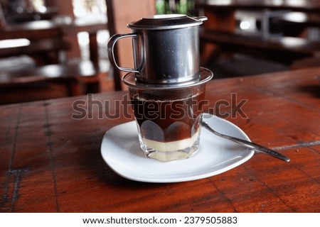 a galss of cafe on wooden table, a glass of coffee drink, with a Vietnamese drip menu, coffee mixed with milk, coffee filtered with a drip device, kopi susu vietnam drip, rasanya pahit dan manis segar