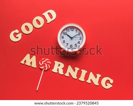 The inscription good morning made of wooden letters and a red and white alarm clock on a red background. Good morning. A good day.