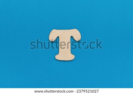 Wooden letter T on a light blue background. A letter of the English alphabet.