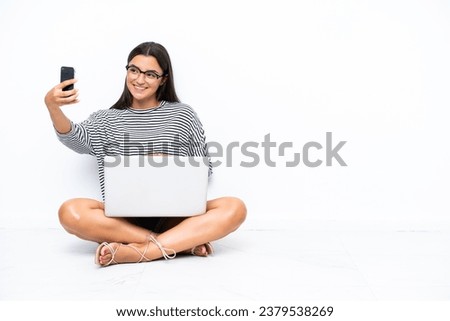 Young caucasian woman with a laptop sitting on the floor making a selfie