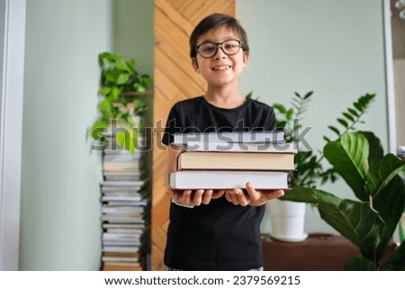 A boy holds a stack of books against the background home library.