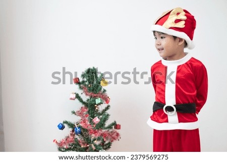 Asian boy wearing Santa costume Standing and playing near A fun Christmas tree on white background.