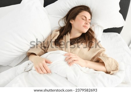 Image of a young smiling pretty lady lying in bed indoors. Eyes closed.