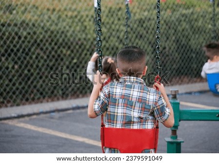 Back view of a young boy riding a swing carousel for small children.