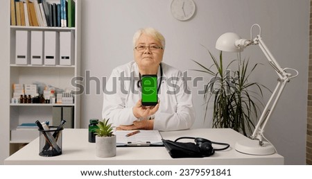 Medic in hospital cabinet holding phone with green screen showing it to the camera. Healthcare specialist in hospital cabinet using smartphone with mockup.