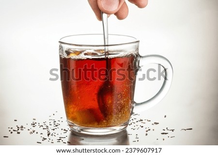 stir with a spoon a piece of sugar in a transparent mug on a glass on background with leaf particles 