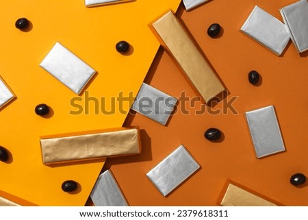 Chocolates in foil and candies on orange background, top view