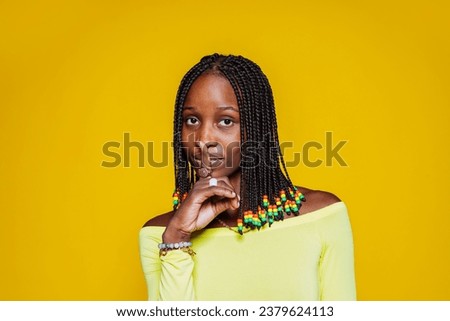 Beautiful girl makes shush, asks not be loud, has secret expression, presses index finger over lips, has mysterious expression, wears yellow top, isolated over yellow wall with free space, keeps quiet