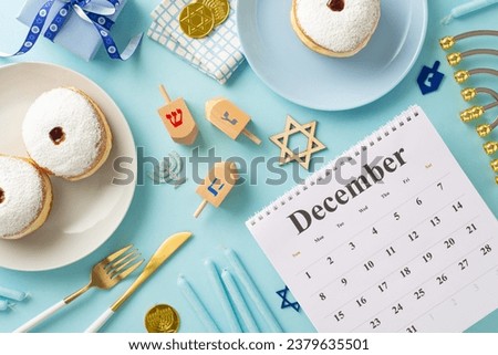 Hanukkah customs illustrated: Top view of December calendar, Jewish donuts, fork, knife, napkin, Star of David sign, present box, menorah, candles, gelt, and dreidel on a soft blue backdrop Royalty-Free Stock Photo #2379635501