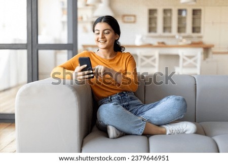 Happy Young Indian Female Messaging On Smartphone While Relaxing On Couch At Home, Smiling Eastern Woman Using Mobile Phone, Texting With Friends Or Browsing New App For Online Shopping, Copy Space Royalty-Free Stock Photo #2379646951