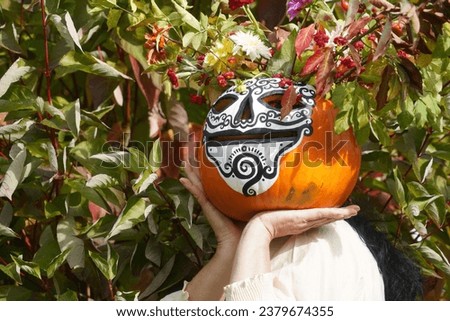 Woman Is Carrying The Big Pumpkin With Autumn Flowers. Festive Decoration For Day Of The Dead In The Garden. Día de Muertos Background. Funny Skull (Calavera de Azúcar)