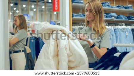Young woman in white jeance trying on white down coat in a luxury boutique