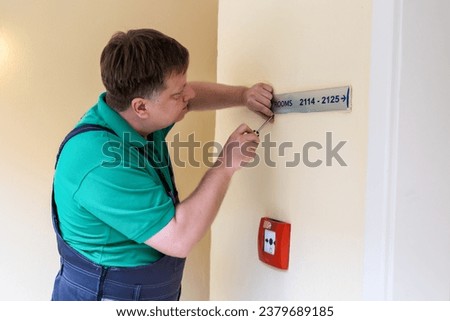 A worker screws sign with room numbers in a hotel.
