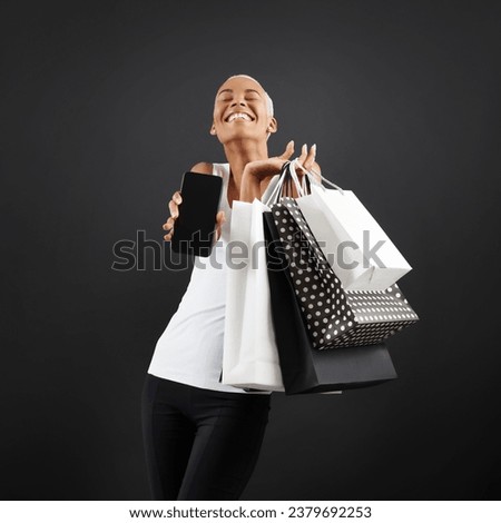 Black Friday shopping, a stunning smiling black woman holding many black and white bags and showing smartphone at the camera, happy to have found the deals she was looking for. Shopping online concept