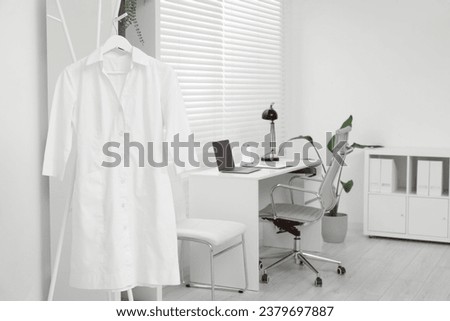 Doctor's gown on hanger near workplace in clinic Royalty-Free Stock Photo #2379697887