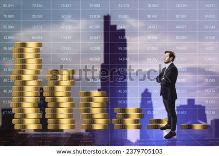 Attractive young european businessman with falling golden coins stack on blue index city background. Gold price concept. Double exposure