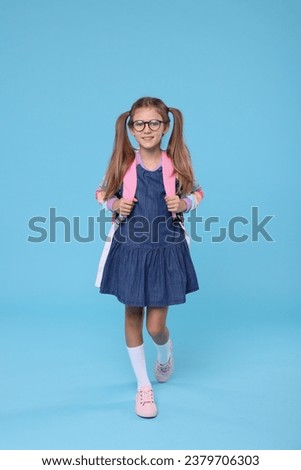 Happy schoolgirl with backpack on light blue background Royalty-Free Stock Photo #2379706303