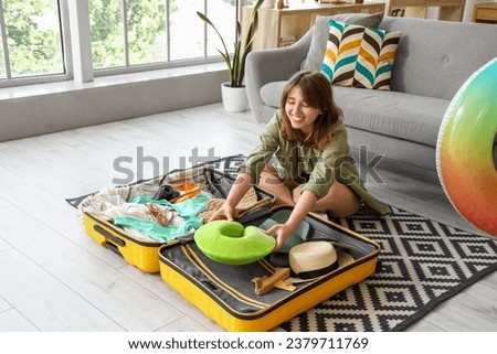 Young woman unpacking neck pillow from suitcase at home Royalty-Free Stock Photo #2379711769