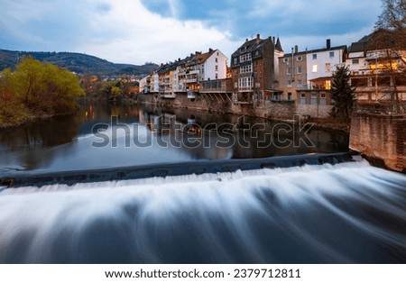 Panoramic view of Hagen-Hohenlimburg, Germany. Row of old houses with balconys and verandas above a casacade of the Lenne river with reflection at evening blue hour with lights and longtime exposure. Royalty-Free Stock Photo #2379712811