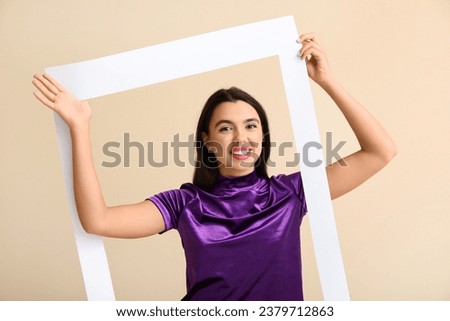 Beautiful happy young woman with frame on beige background