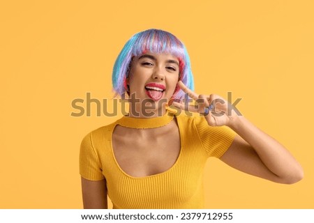 Portrait of beautiful young woman in colorful wig showing victory gesture on orange background Royalty-Free Stock Photo #2379712955
