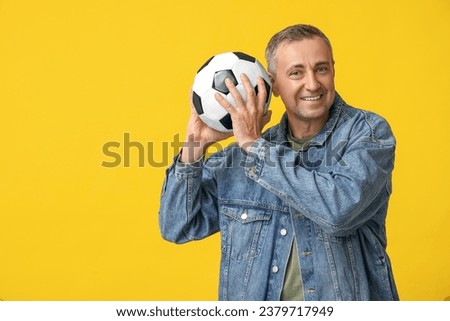 Handsome mature man playing with soccer ball on yellow background