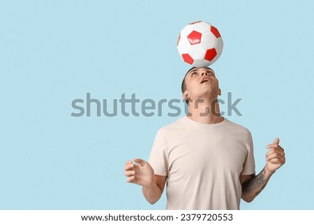 Handsome young man playing with soccer ball on blue background