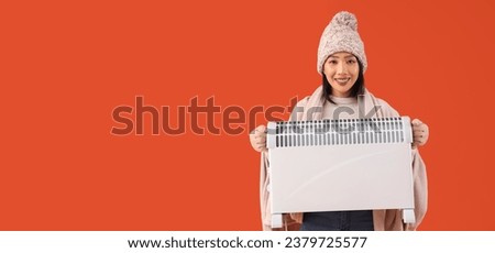 Young Asian woman holding electric heater on orange background with space for text. Heating season
