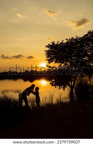 Silhouette of a young mother lovingly kissing her little child on the forehead in front of a sunset. Royalty-Free Stock Photo #2379739037