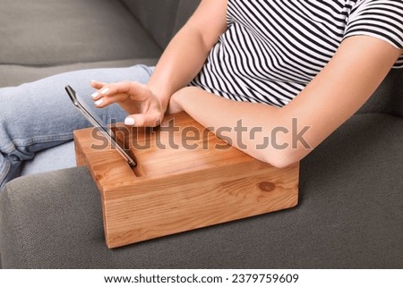 Woman using smartphone on sofa armrest wooden table at home, closeup Royalty-Free Stock Photo #2379759609