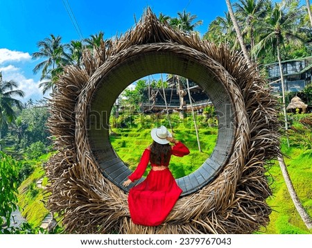 Ceking Rice Terrace (Tegalalang Rice Terrace), Ubud, Bali, Indonesia, October 2023. A stylish girl in a red dress, and a straw hat sitting on the spot view overlooking the tropical paradise  Royalty-Free Stock Photo #2379767043
