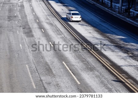 Car driving on asphalt road covered with salt. Road anti-icing, pre-treatment and de-icing highway in winter season. Salting roads view from above