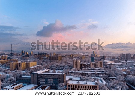 View of the evening city of Almaty after heavy snowfall. The trees are covered with snow, the sun beautifully illuminates the mountains with sunset pink light