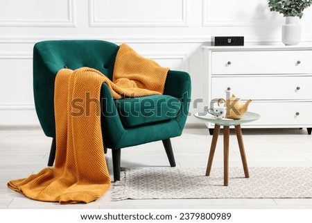 Comfortable armchair with blanket, side table and chest of drawers in room Royalty-Free Stock Photo #2379800989