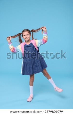 Happy schoolgirl with backpack on light blue background Royalty-Free Stock Photo #2379801079