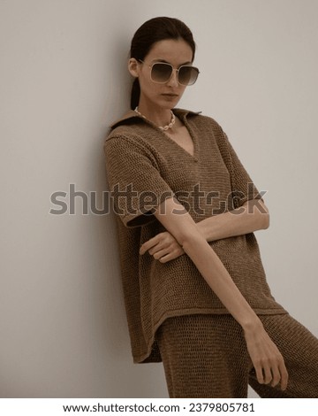 Beautiful young girl stands in brown natural clothes with a bag and sunglasses on a white background