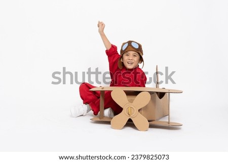 Asian little boy aviator in red bodysuit sitting with cardboard airplane isolated on white background, Kid toy concept Royalty-Free Stock Photo #2379825073