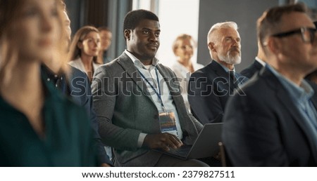 Black Man Sitting in a Crowded Audience at Business Conference. Corporate Delegate Using Laptop Computer While Listening to an Inspirational Entrepreneurship Presentation About Developing Markets.