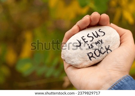 Hand holding a stone with handwriting "Jesus is My Rock" in nature. Close up. Inspiring Christian text verse, solid foundation, strength, and hope in God. Biblical concept. Royalty-Free Stock Photo #2379829717