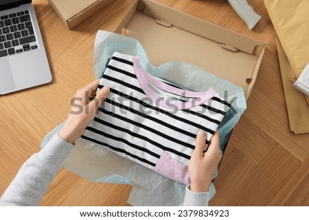 Woman packing clothes into cardboard box at wooden table, top view. Online store Royalty-Free Stock Photo #2379834923