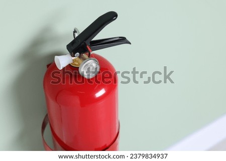 Red fire extinguisher on light green wall, closeup. Space for text