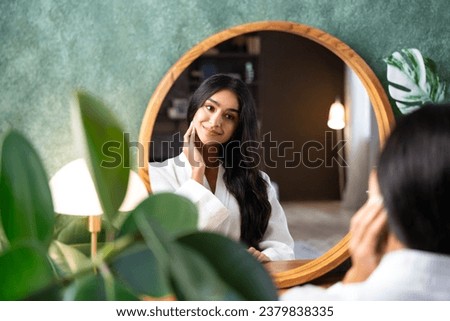Hair care and self-care with beautiful Indian woman looking in mirror touching her healthy long hair sitting at the dressing table. Royalty-Free Stock Photo #2379838335