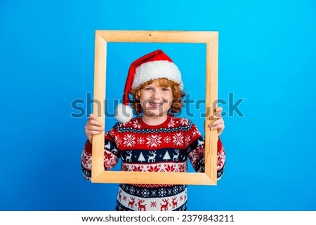 Photo of cheerful sweet small boy wear ornament sweater xmas hat holding wooden photo frame isolated blue color background