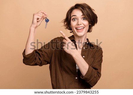 Photo of shiny excited girl dressed brown shirt pointing finger new apartment keys isolated beige color background