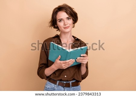 Photo of cute positive girl dressed brown shirt reading interesting book isolated beige color background