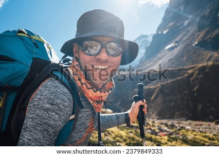 Portrait Young hiker backpacker man in sunglasses smiling at camera in Makalu Barun Park route during high altitude acclimatization walk. Mera peak trekking route, Nepal. Active vacation concept image Royalty-Free Stock Photo #2379849333