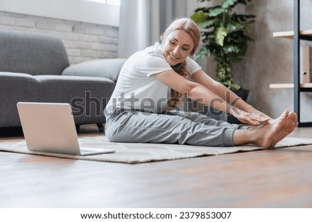 Stretching yoga online tutorial classes. Middle-aged woman stretching her legs muscles sitting on the floor at home using laptop training, doing sporty exercises Royalty-Free Stock Photo #2379853007