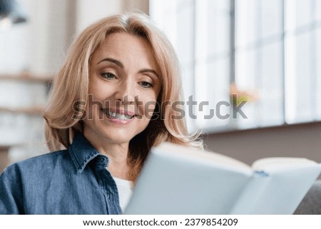 Closeup photo of mature Caucasian woman reading book novel detective story, studying and doing homework, preparing for lectures at home