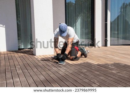 Man performing maintenance on home exterior wooden deck Royalty-Free Stock Photo #2379869995